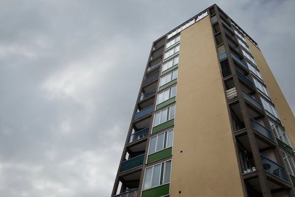 Flatgebouw in beige en groen, met hoekbalkons en ramen waarin de bewolkte lucht weerspiegelt.