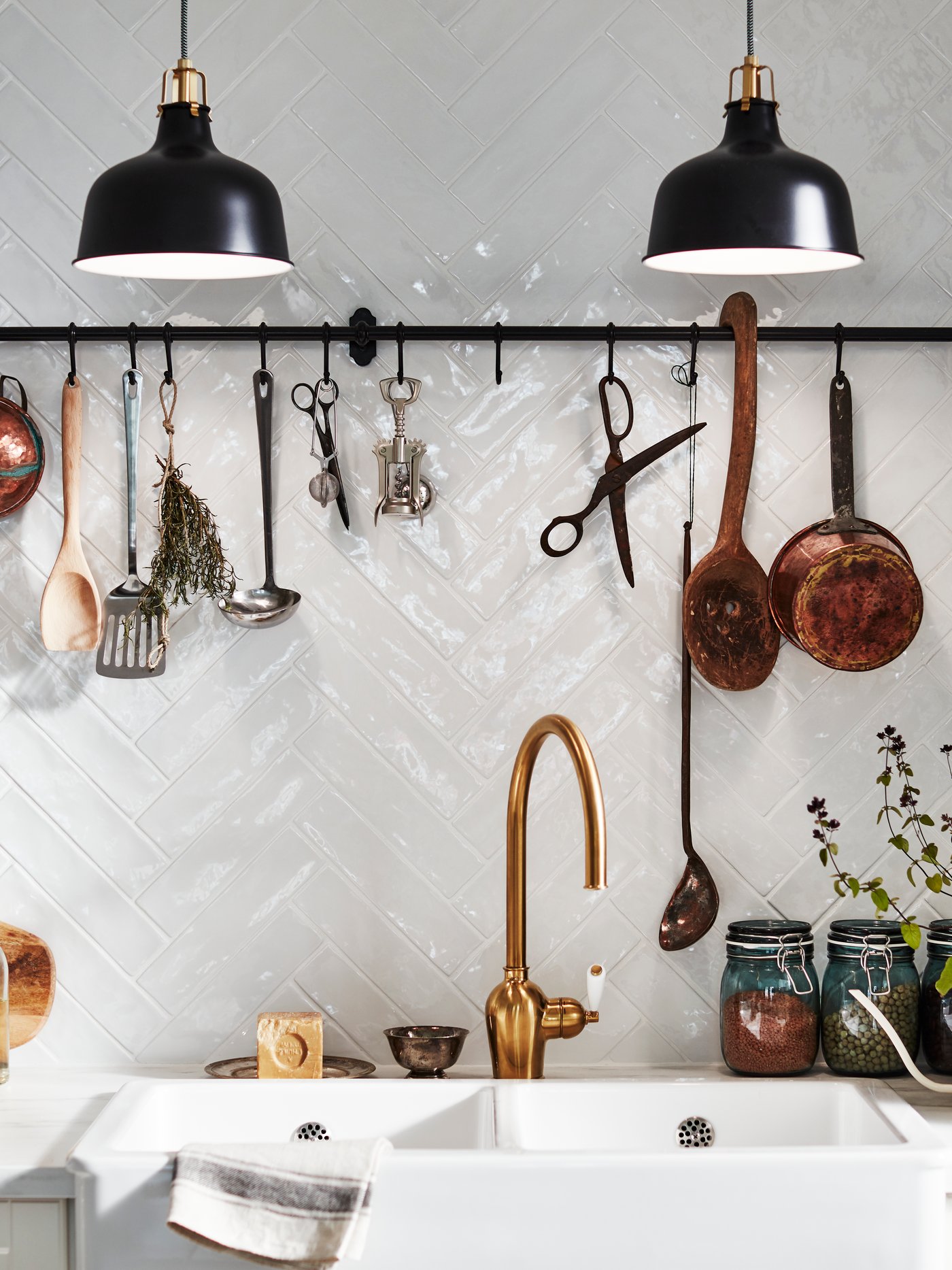 A FINTORP rail with hooks on a tiled wall above a sink. Herbs, kitchen utensils and decorative items hang from the rail.