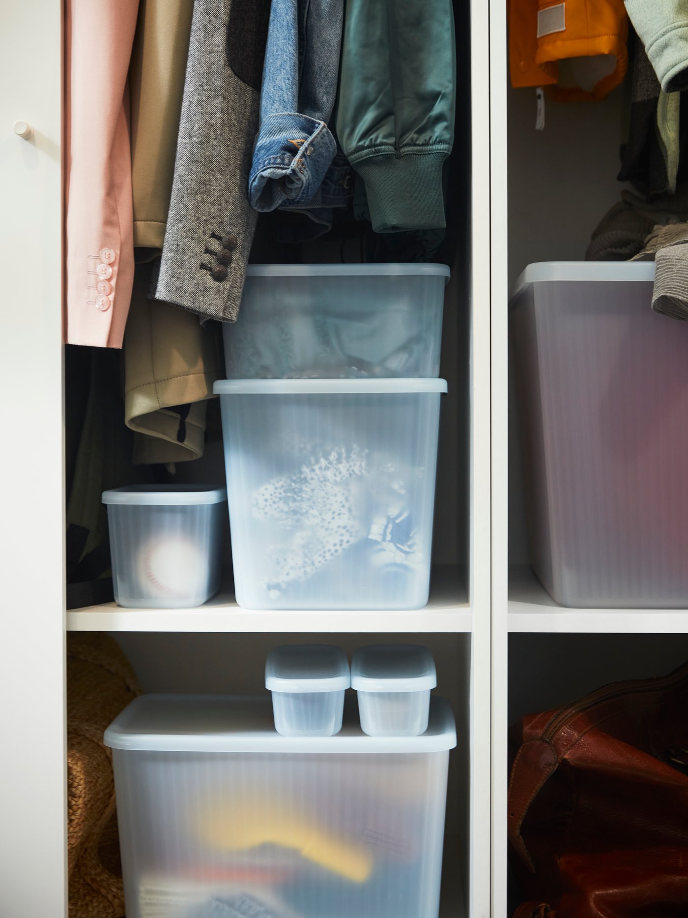 Different sizes of RYKTA storage boxes in a white PAX wardrobe frame with clothing items and other items neatly stored inside. 