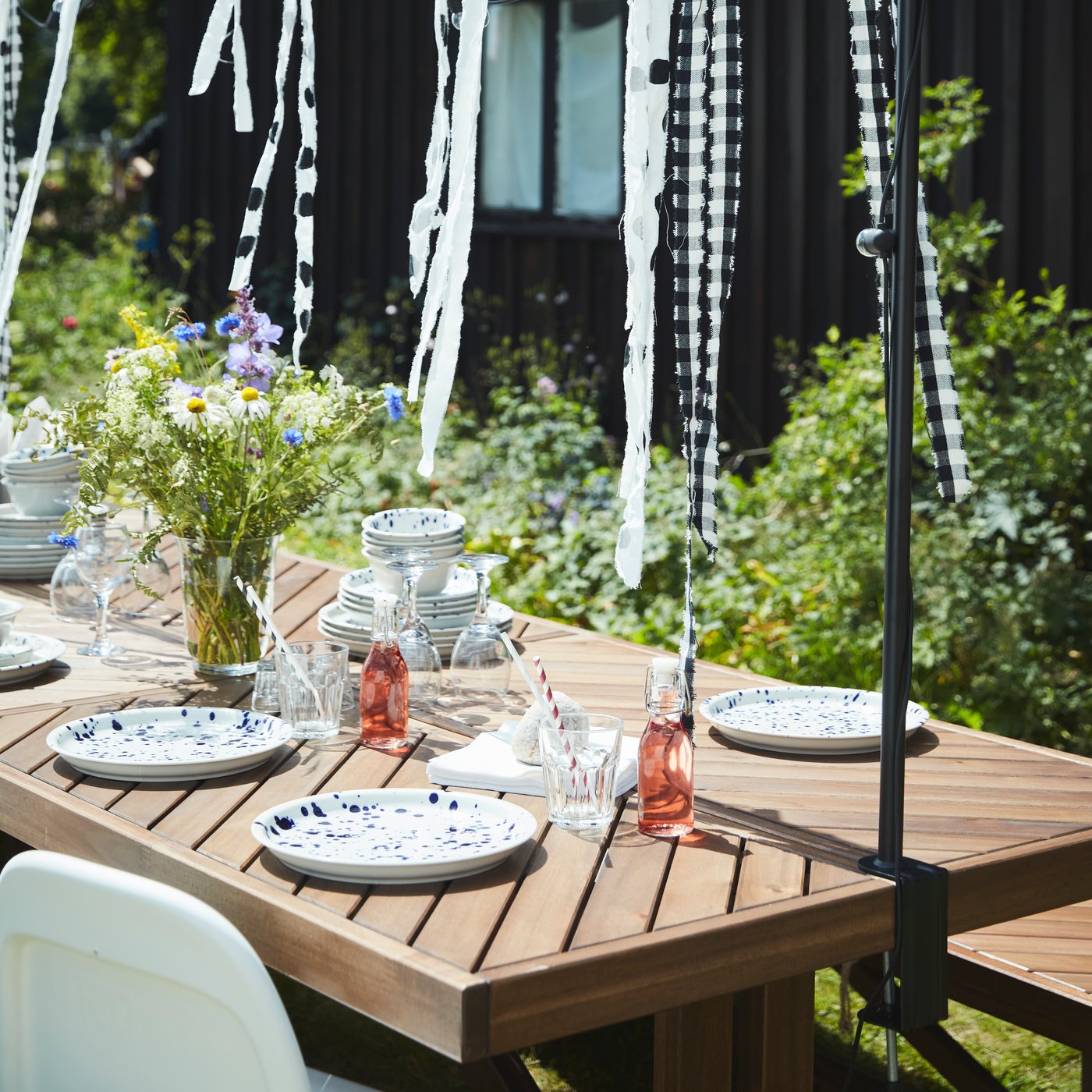 שולחן עץ NORRMANSÖ בגינה ערוך ומקושט לקראת חגיגות אמצע הקיץ.