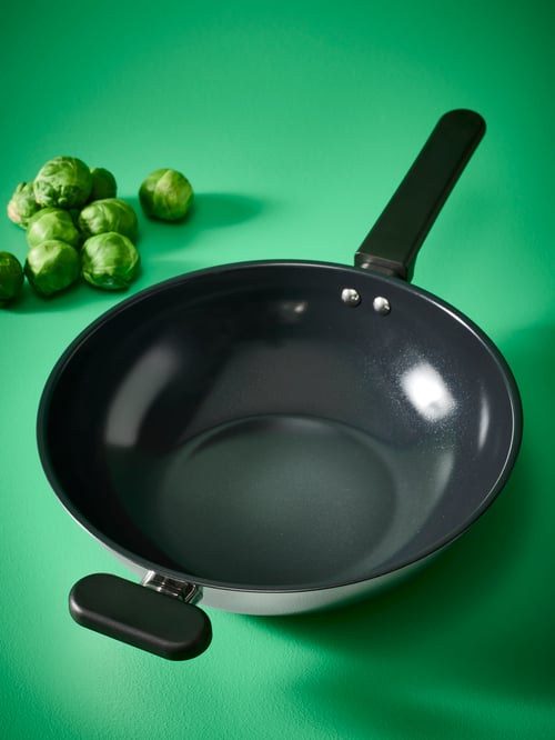 Pe un fundal verde, există un wok MIDDAGSMAT din oțel inoxidabil negru.
