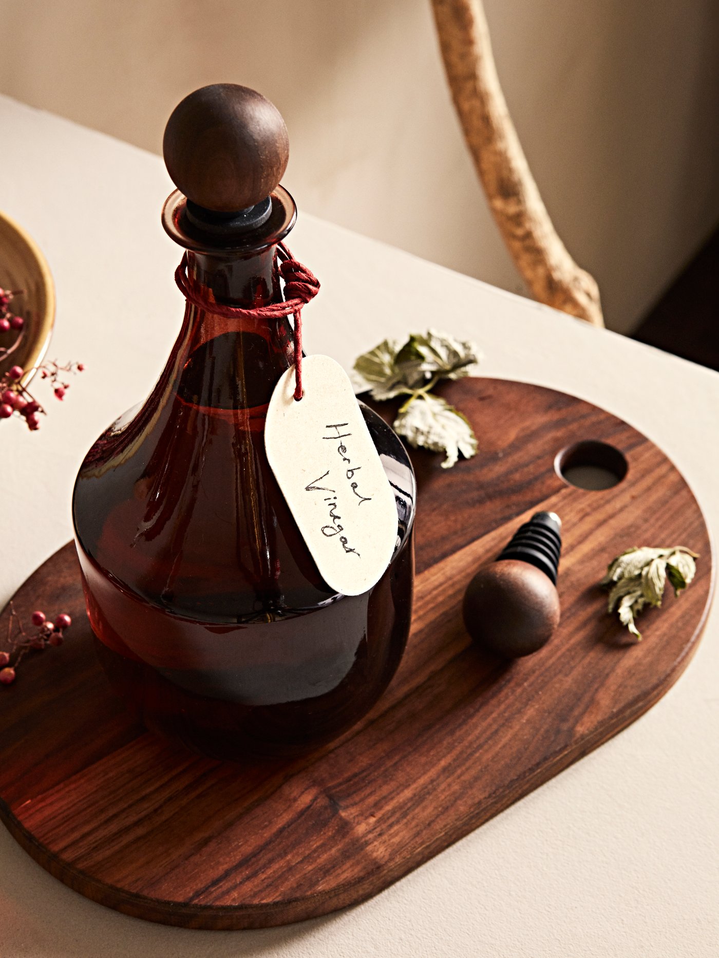 Botol kaca dengan penyumbat kayu KRÖSAMOS yang berlabel terletak di atas papan hidangan kayu KRÖSAMOS.