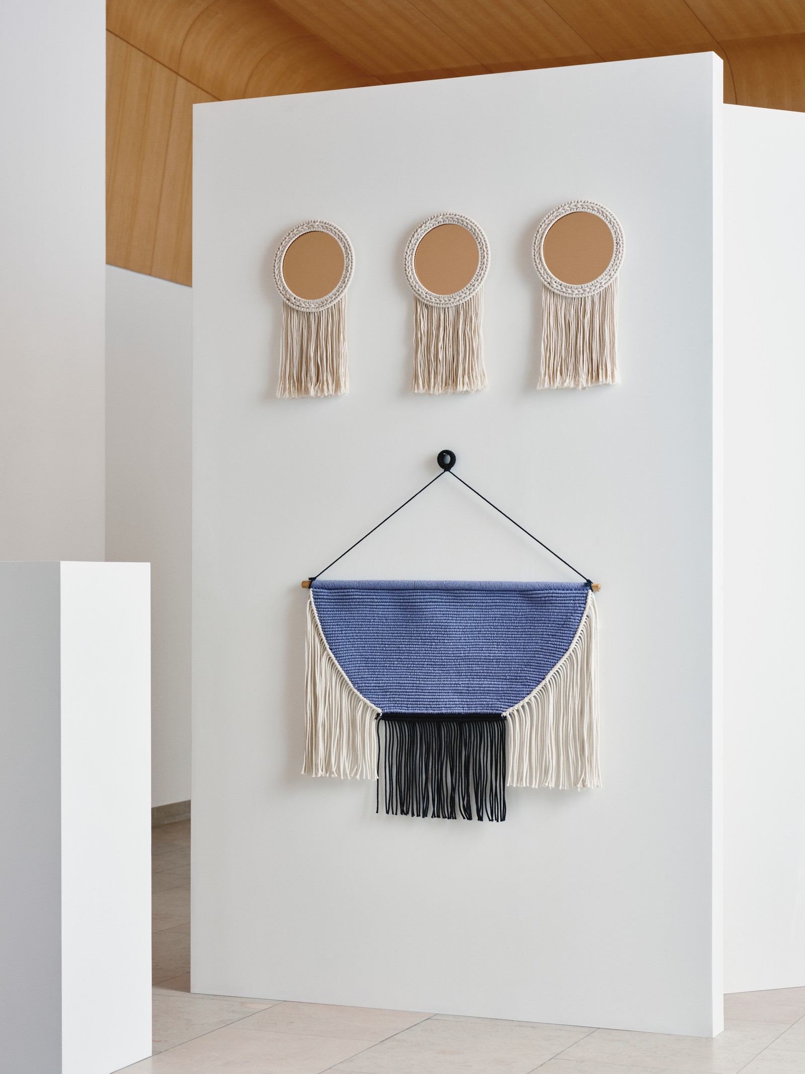 A HÄNGALM wall tapestry in beige black/light lilac-blue hangs from a white wall, undeeath three ENERGISKOG mirrors.