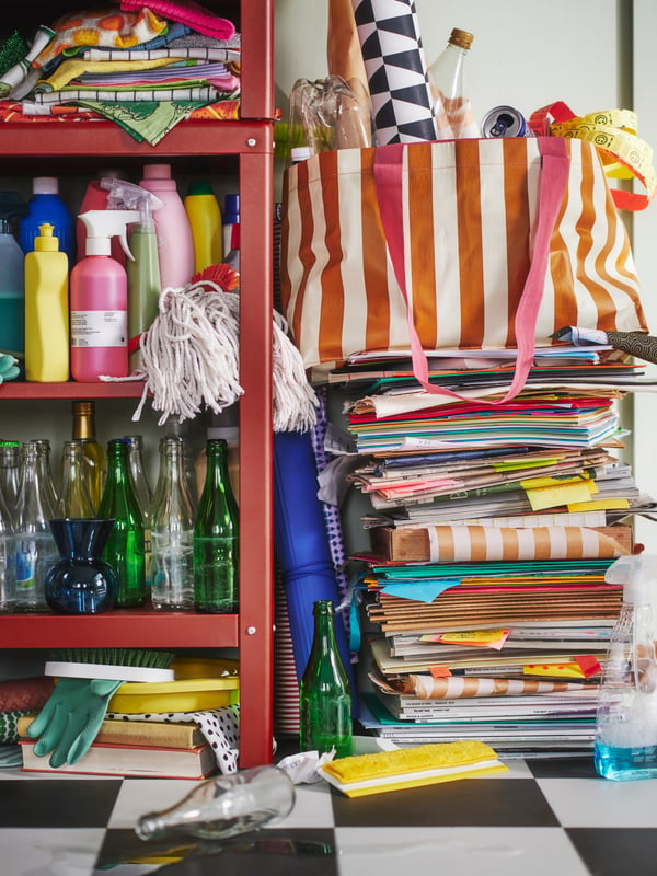 Étagère KOLBJÖRN garnie de bouteilles et de textiles pliés, à côté d’un sac SÄCKKÄRRA posé sur une pile de magazines.