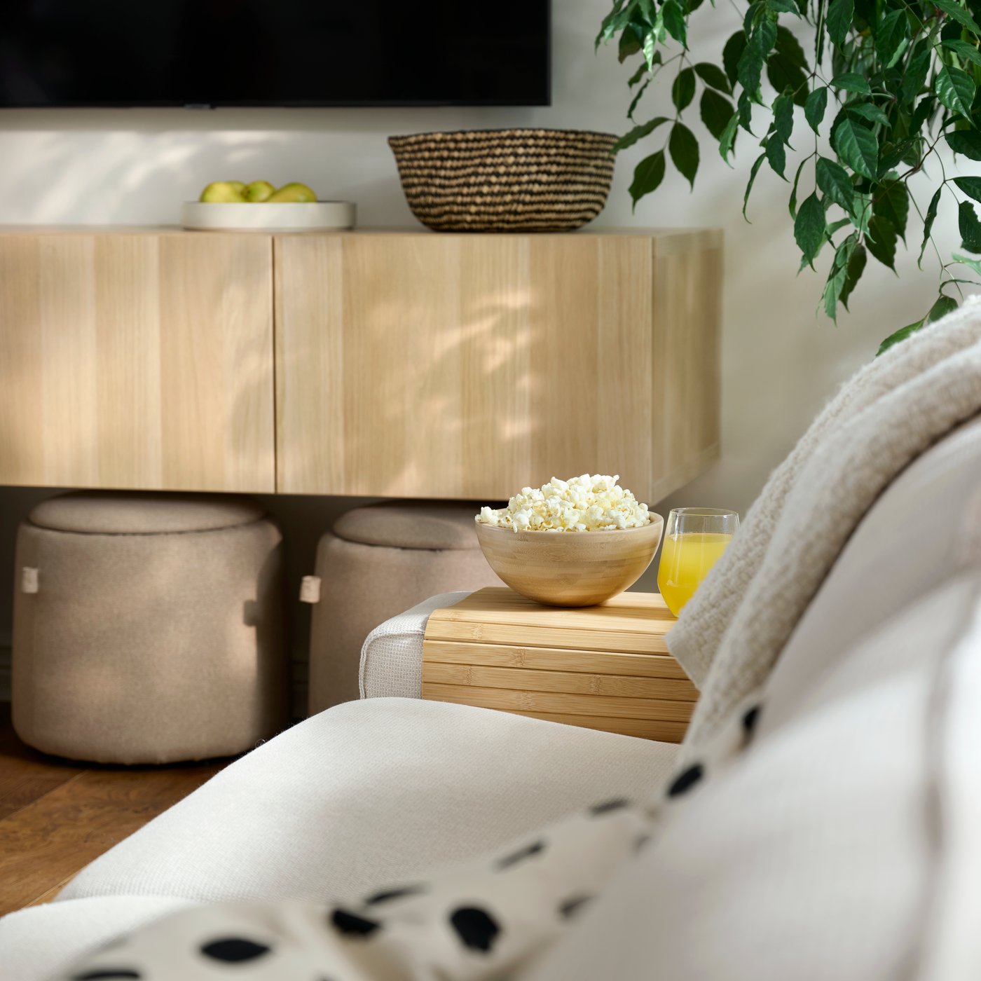 Snacks and a glass of juice rest on a RÖDEBY armrest tray placed the end of a KIVIK sofa in a bright living room.