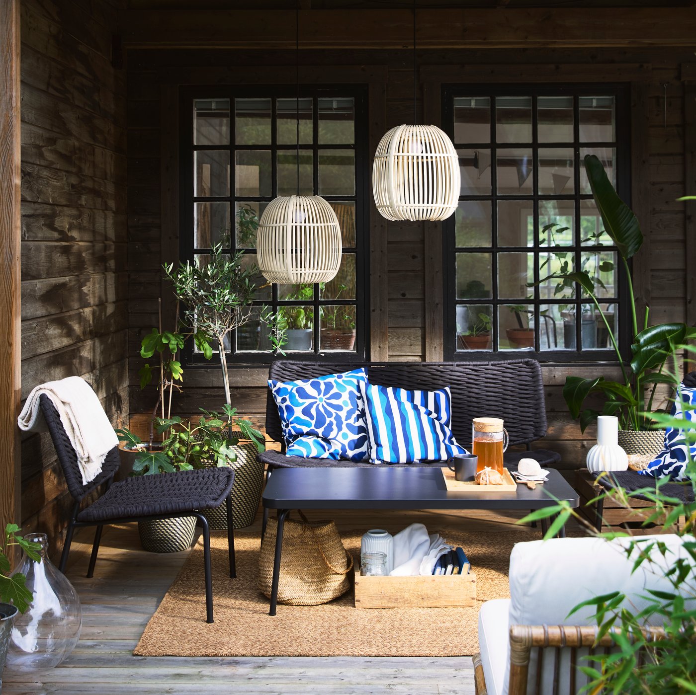 A cozy terrace with black TEGELÖN lounge furniture, blue and white pillows, and decorative SOLVINDEN lighting.