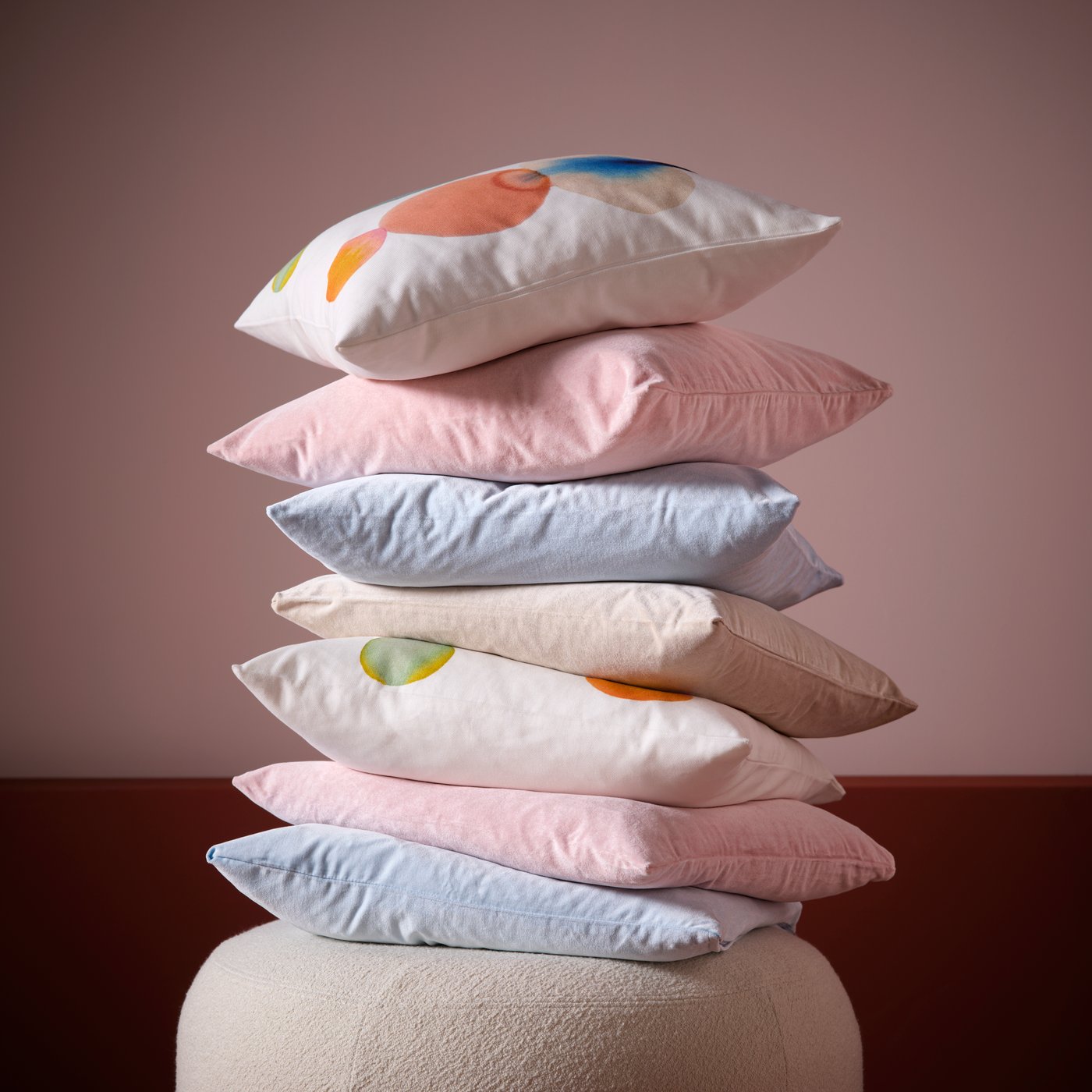 A pile of cushions with different-coloured SANELA cushion covers and multicoloured IKEA PS cushion cover.