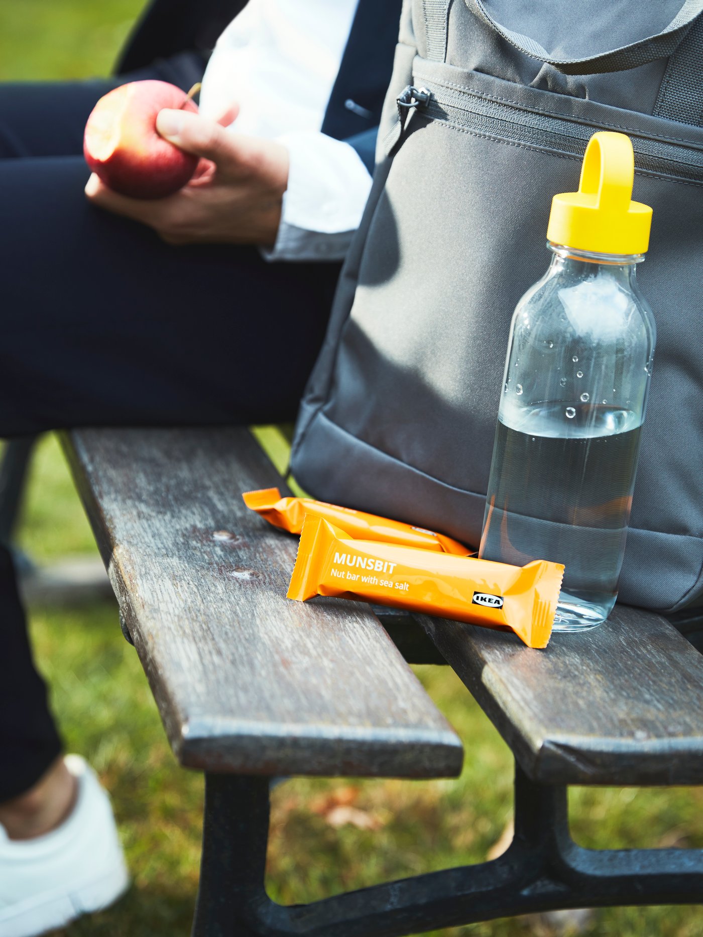 Una persona que lleva una chaqueta azul y una camisa blanca sentada junto a barritas energéticas MUNSBIT, una mochila STARTTID y una botella de agua FORMSKÖN.