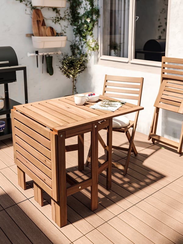 Un balcone soleggiato con un tavolo allungabile. Sopra una tazza GLADELIG. Sullo sfondo un barbeque a carbonella GRILLSKÄR.