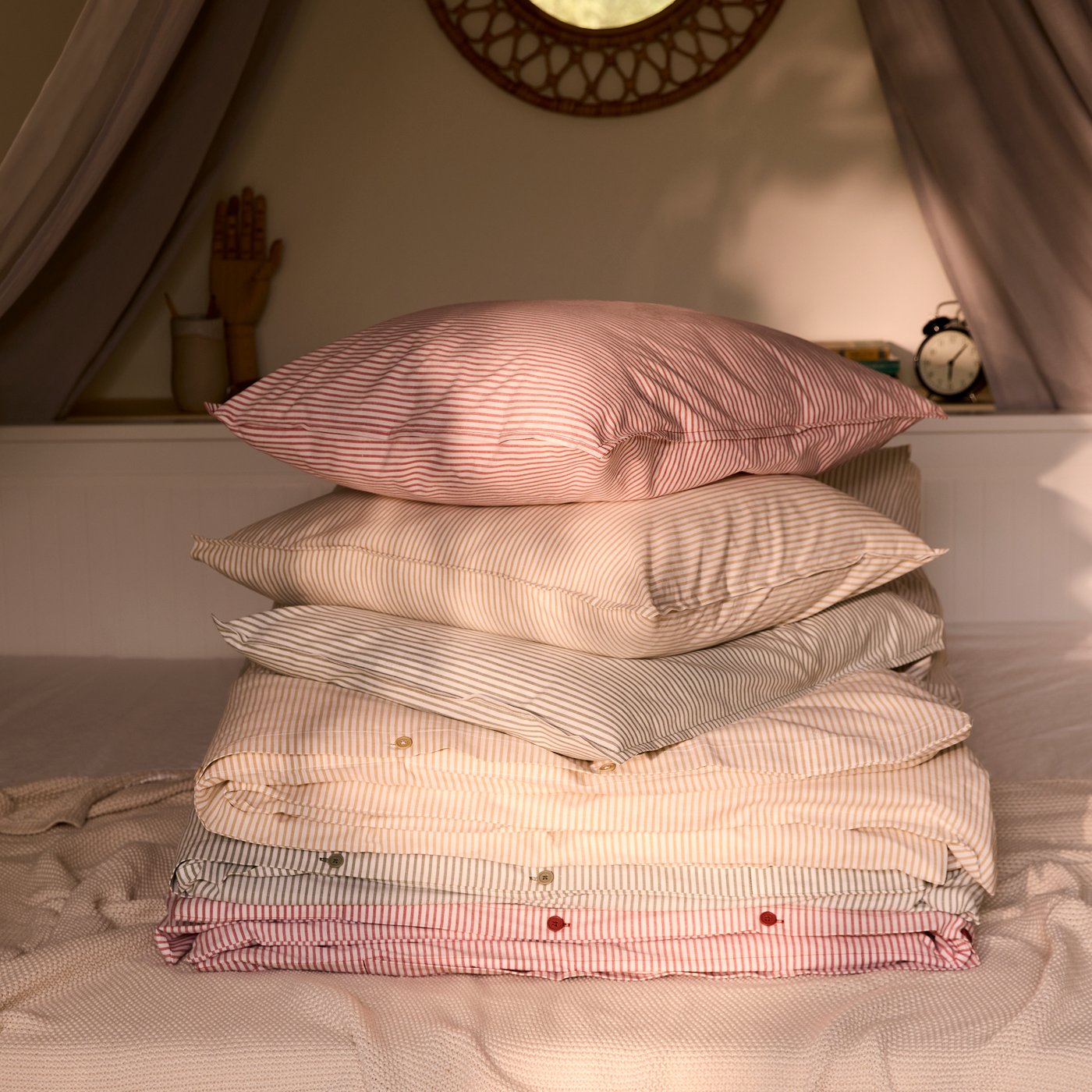 Una pila di copripiumini e cuscini SOLFIBBLA a righe in rosso, blu e giallo, sopra il divano letto HEMNES.