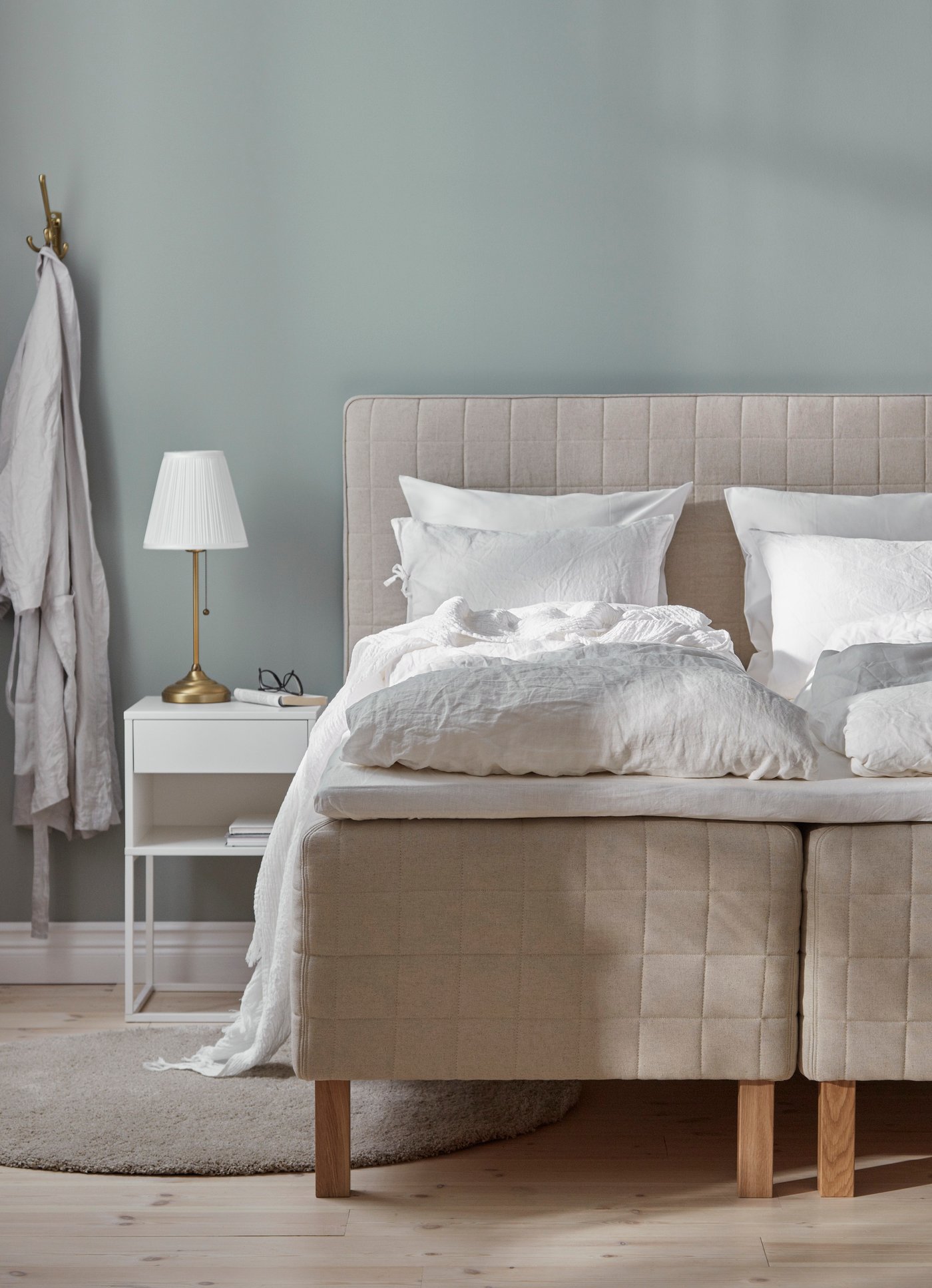 En stor seng av rammemadrasser i et lyst soverom, med hvitt nattbord.