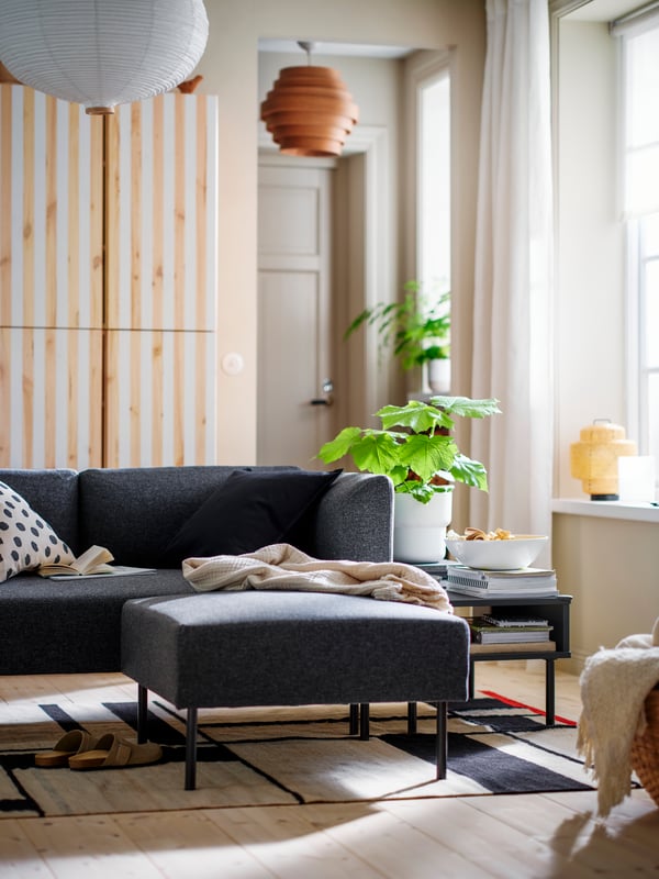 A TUNSTA side table with a plant in a pot on top stands on a RASTPLATS rug at the side of some modular LILLEHEM seating.