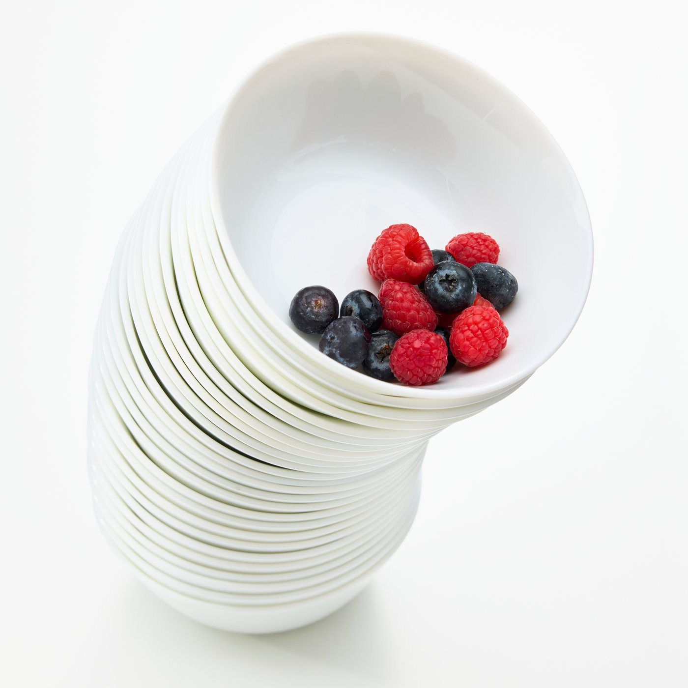 A tall stack of white OFTAST bowls, with some raspberries and blueberries in the top bowl.