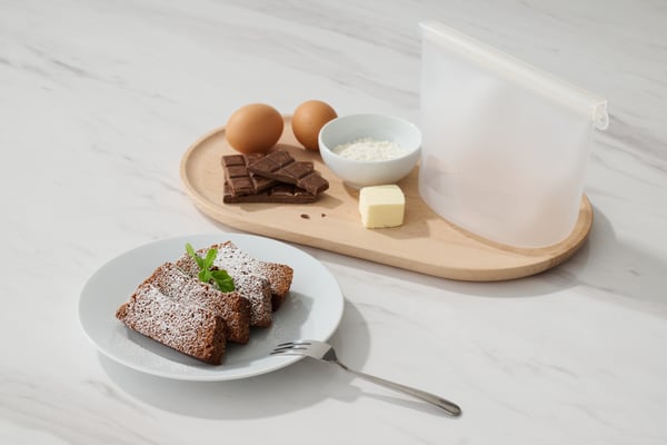 粉糖をふったチョコレートケーキと卵やバターなど焼き菓子の材料、シリコン保存袋が並ぶキッチンシーン