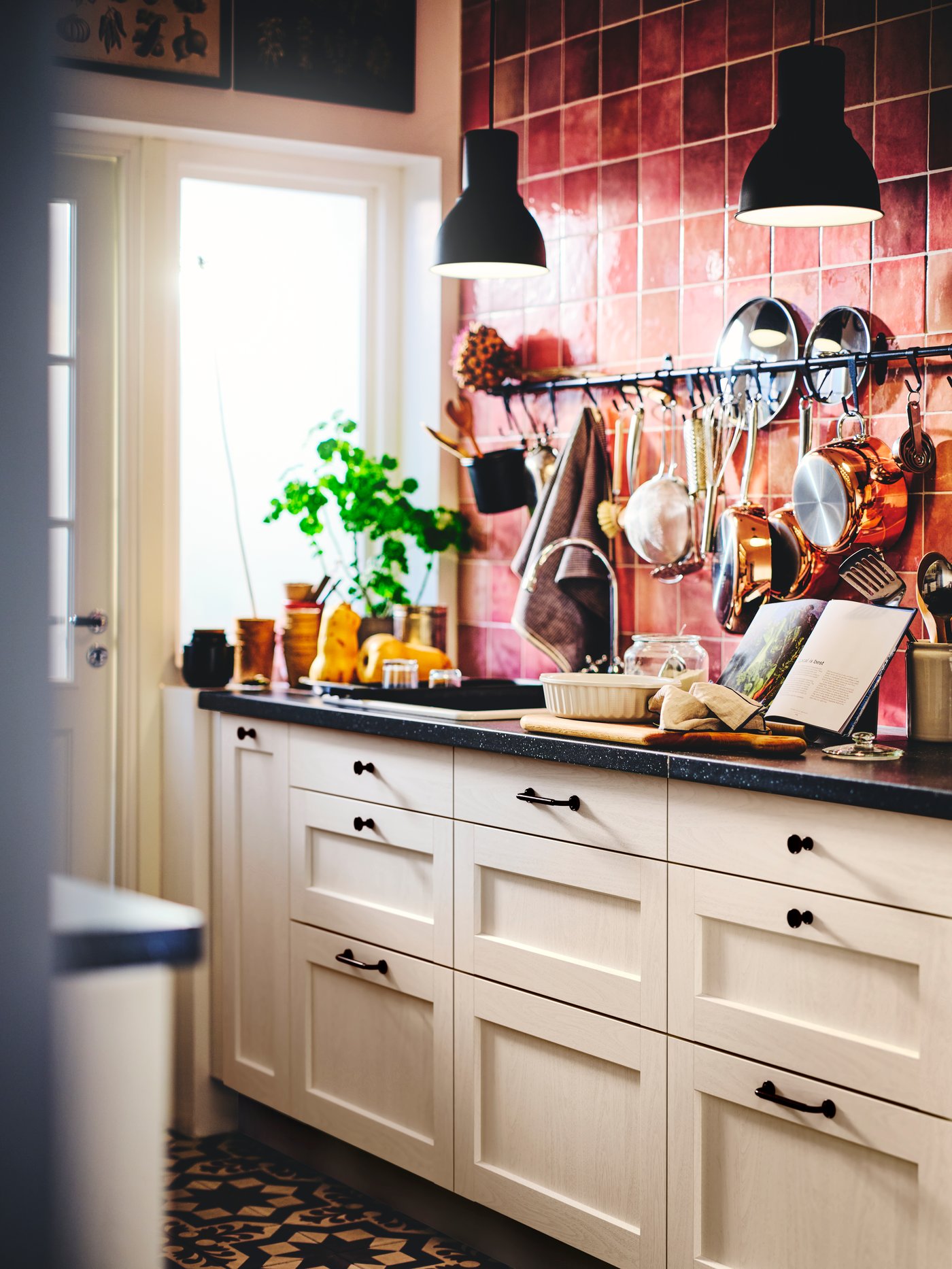 Una cocina con muebles de cocina blancos. En la pared se observa un organizador de pared HULTARP y de sus ganchos cuelgan artículos de cocina, cucharones y otros accesorios.