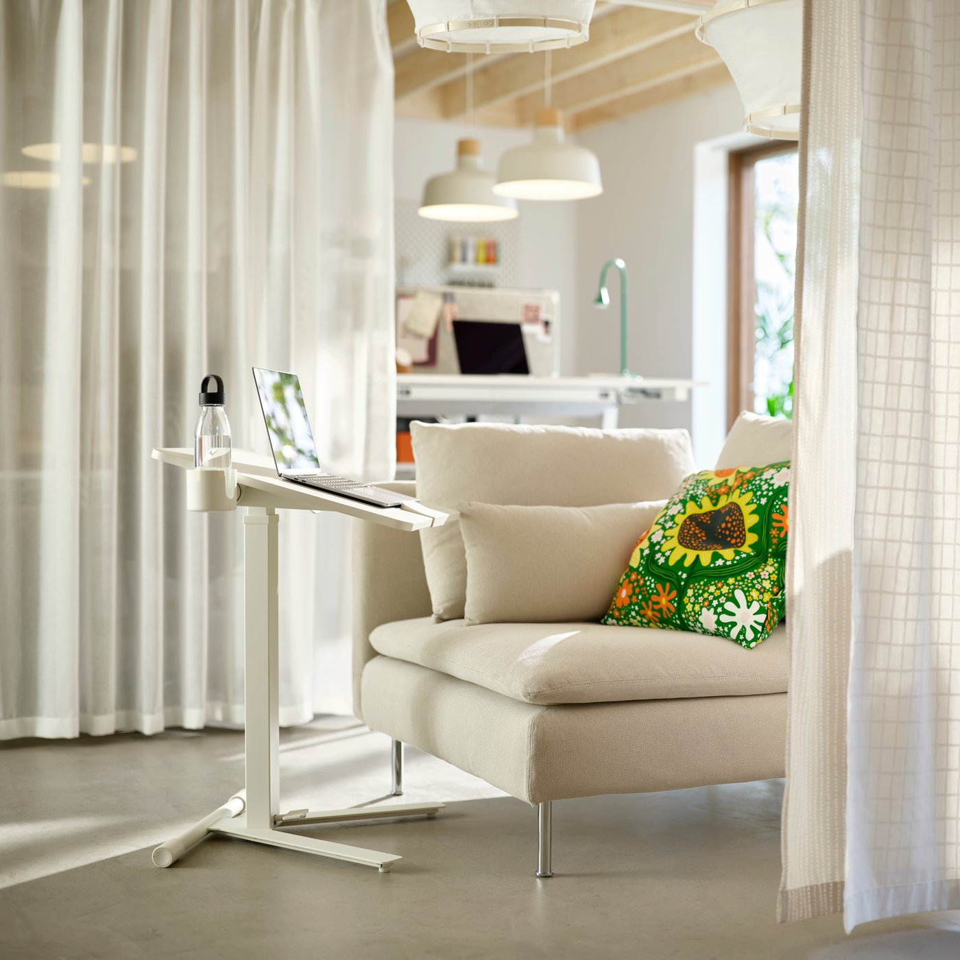 Single white sofa unit with deskstand holding a laptop. Communal workspace in background; divider curtains on either side.