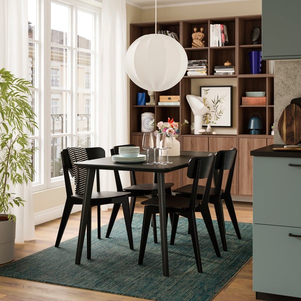 Cozy dining area featuring a black table with chairs, a modern light fixture, potted plant, and a stylish wood shelving unit.