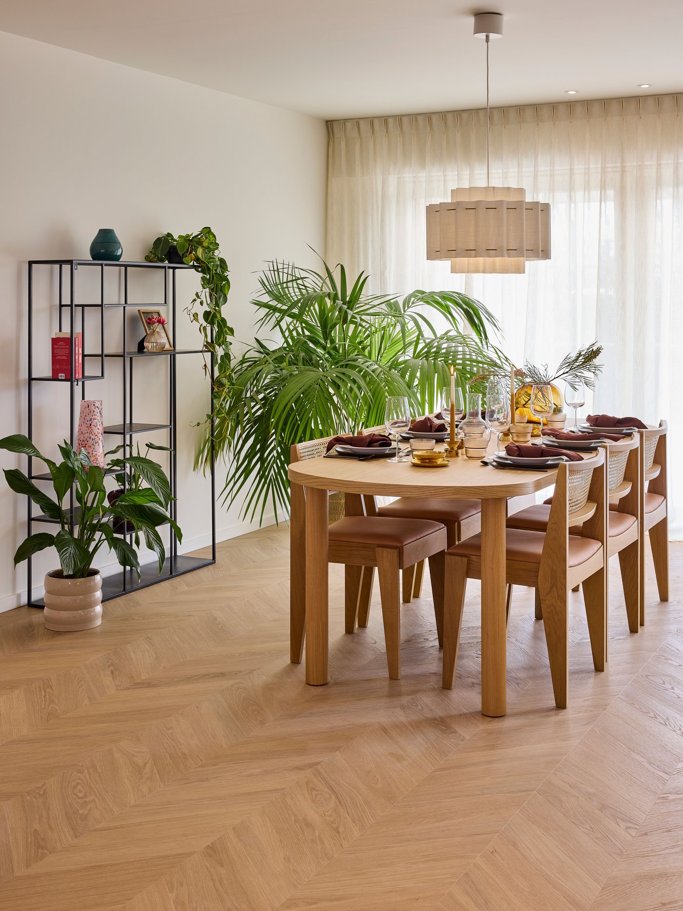 Eetkamer met ronde tafel, stoelen, planten en rek in een lichte ruimte met houten vloer.