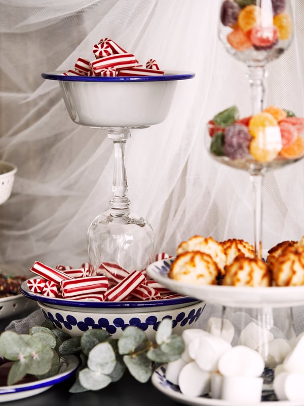 A creative display of plates, glasses and bowls, glued on top of each other, and filled with different types of sweets.