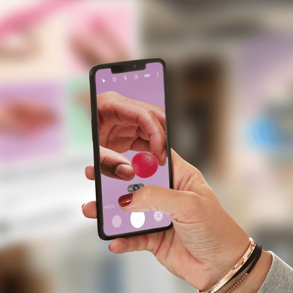 Dłoń fotografuje czerwony żelek smartfonem