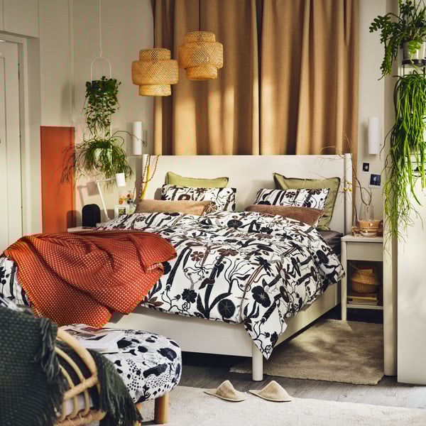 An off-white TONSTAD bed in a bright bedroom covered with white/black/brown LUNDSKAFTING bed linen and a rust throw.
