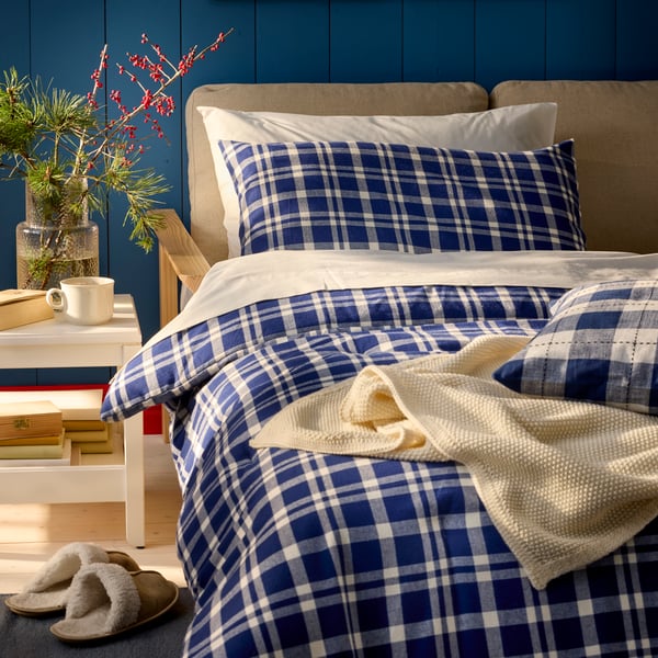 A dark blue TORNTUSS comforter set adorns a neatly made bed with matching pillows, accented by a cosy throw.