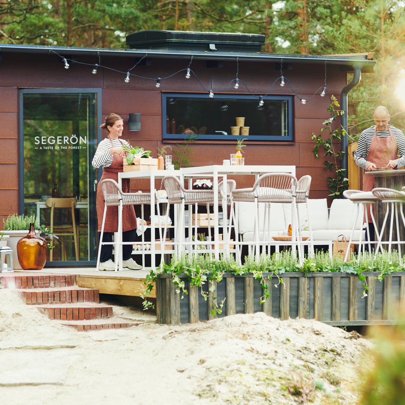 Two people are setting up an outdoor pop-up restaurant in the forest consisting of SEGERÖN outdoor furniture.