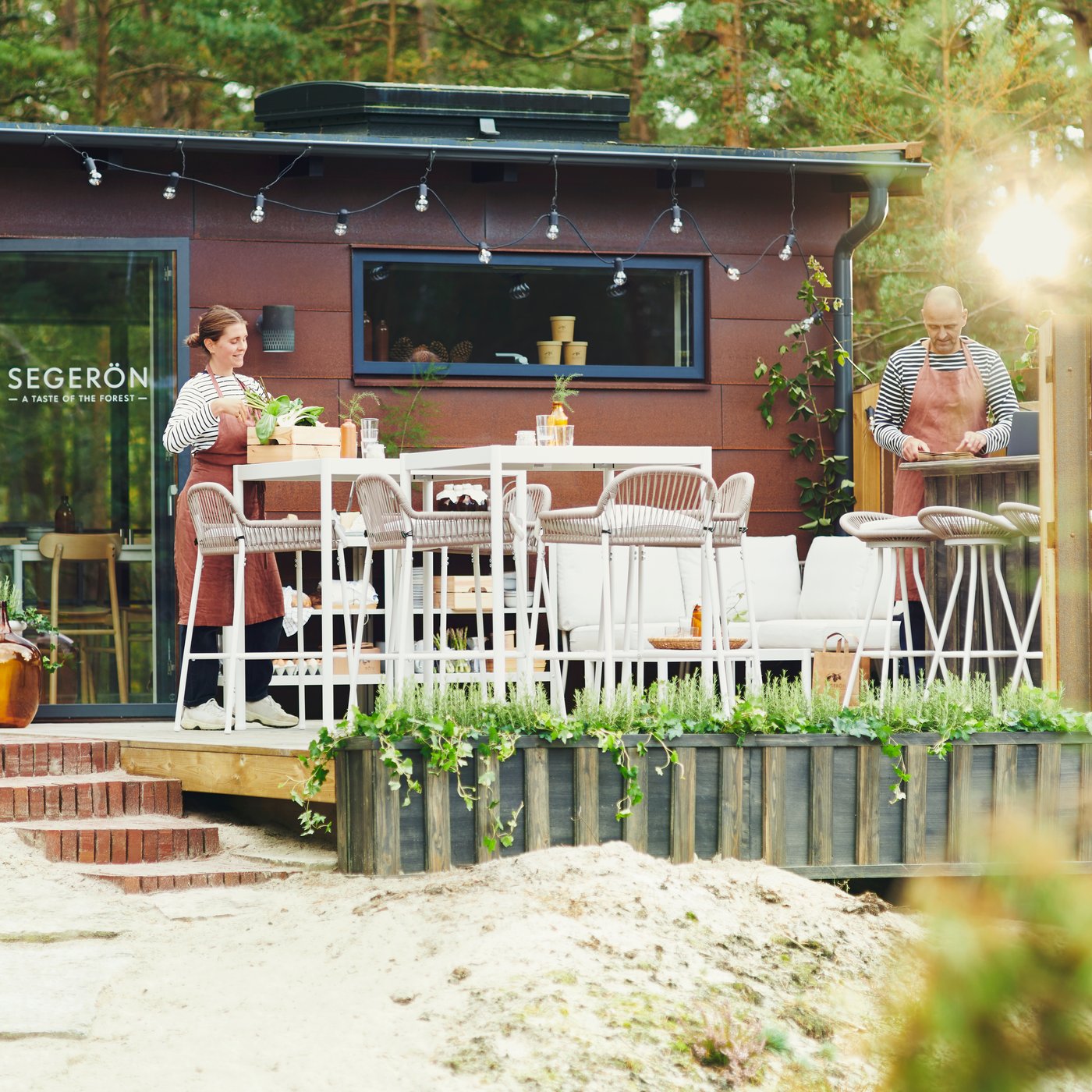 In un ristorante nella foresta, due persone stanno sistemando i mobili da esterno SEGERÖN.