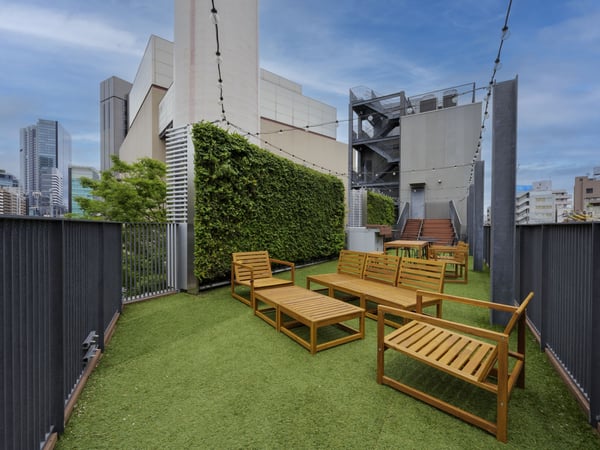 木製ベンチが並ぶ屋上スペース。高層ビルと緑の壁が背景に広がるリラックス空間