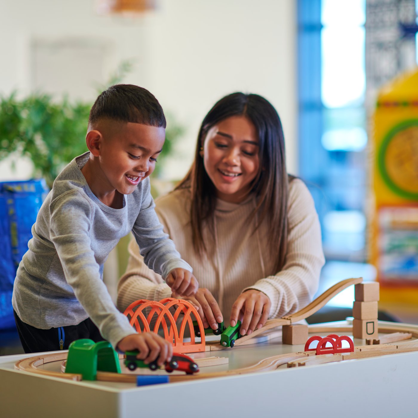 Nainen ja lapsi leikkivät junaratapöydän äärellä.