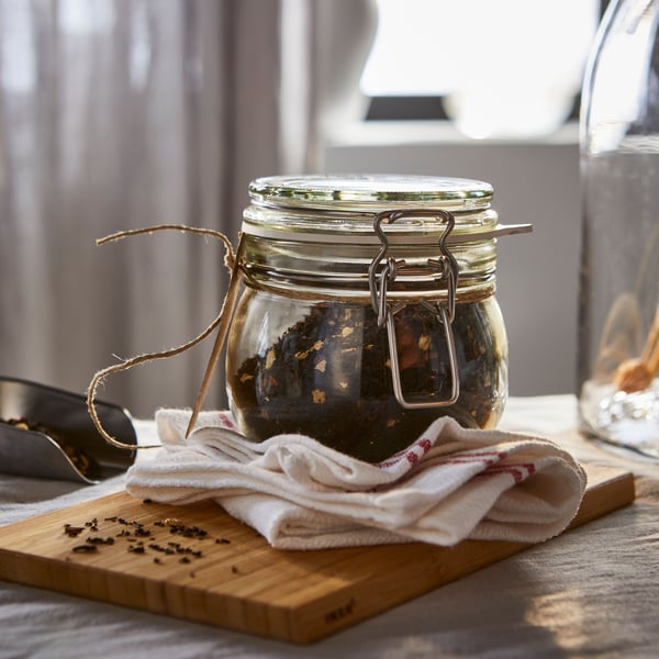 A KORKEN jar with lid filled with a mix of dried ingredients stands on a tea towel on top of an APTITLIG chopping board.