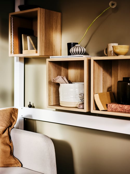 Trois armoires beiges contenant un sablier décoratif, un vase blanc et plusieurs livres sont fixées au mur.