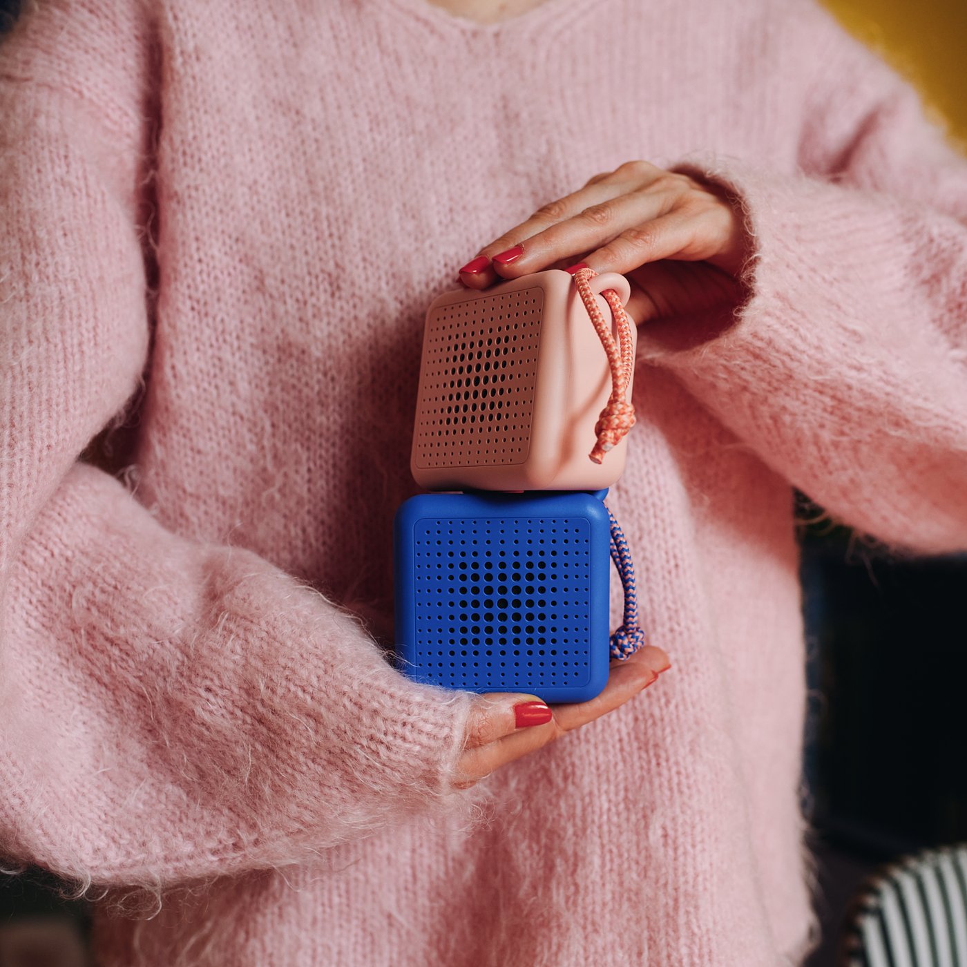 Someone in a pink sweater is holding a waterproof VAPPEBY portable Bluetooth speaker in pink and blue.