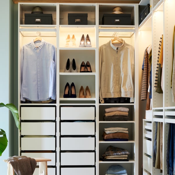 An open PAX system, with integrated lighting, showing off hanging shirts, neatly folded sweaters and shoes put on display.