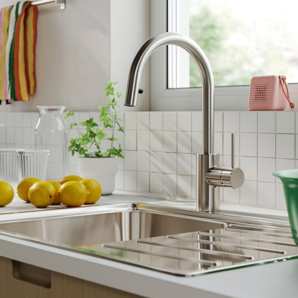 A bright kitchen counter top with natural light from a window, white tiles and a SALLSJÖN kitchen mixer tap.