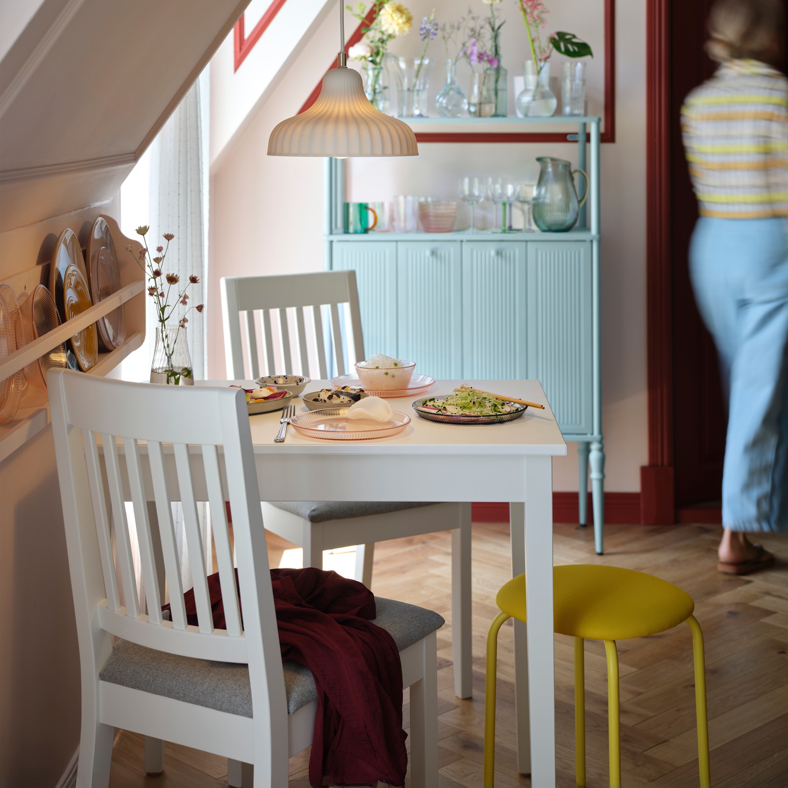 A white NÄSINGE table stands elegantly in a bright dining area with a light grey-blue SÅGMÄSTARE cabinet in the background.