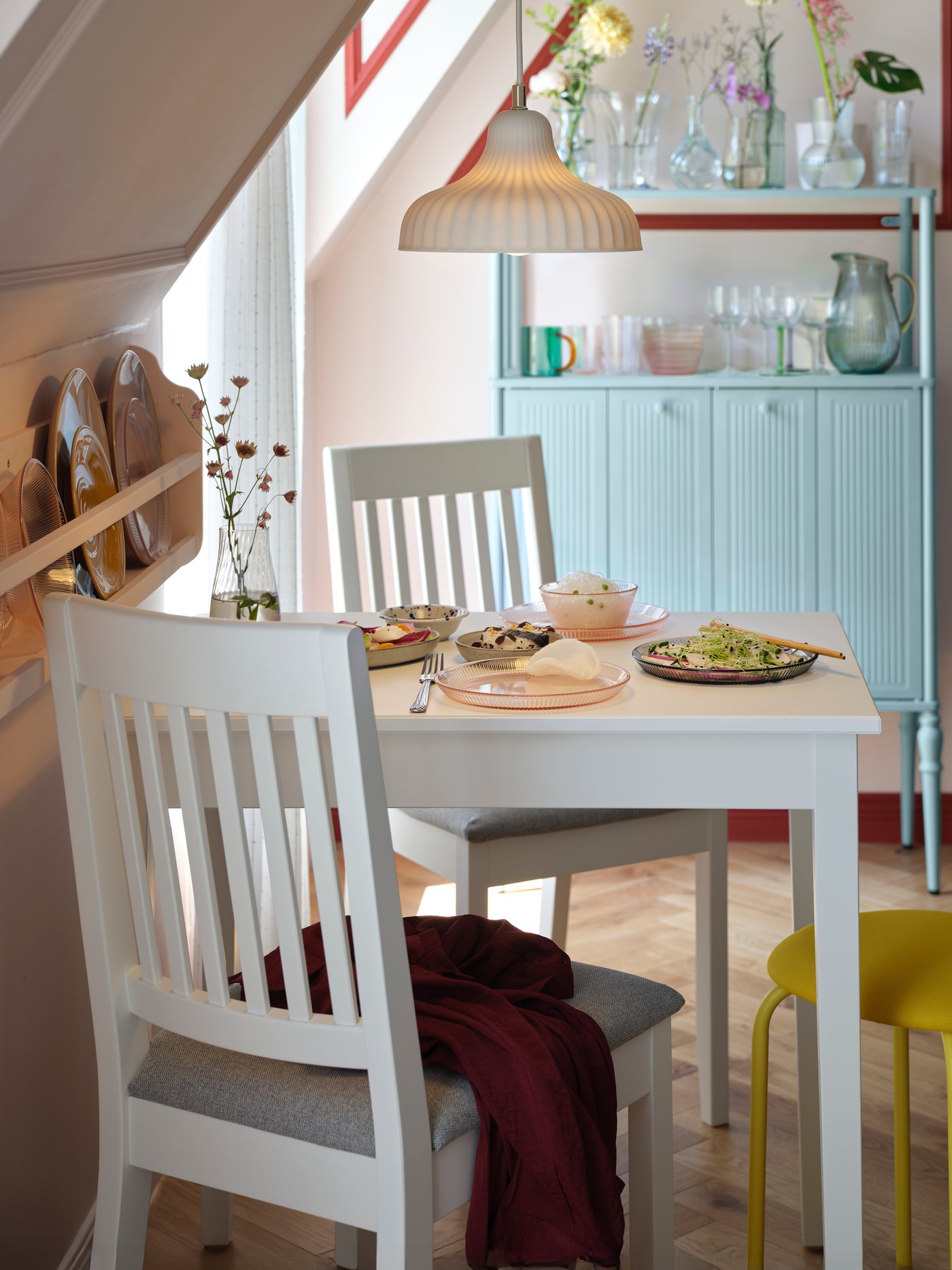 A white NÄSINGE table stands elegantly in a bright dining area with a light grey-blue SÅGMÄSTARE cabinet in the background.