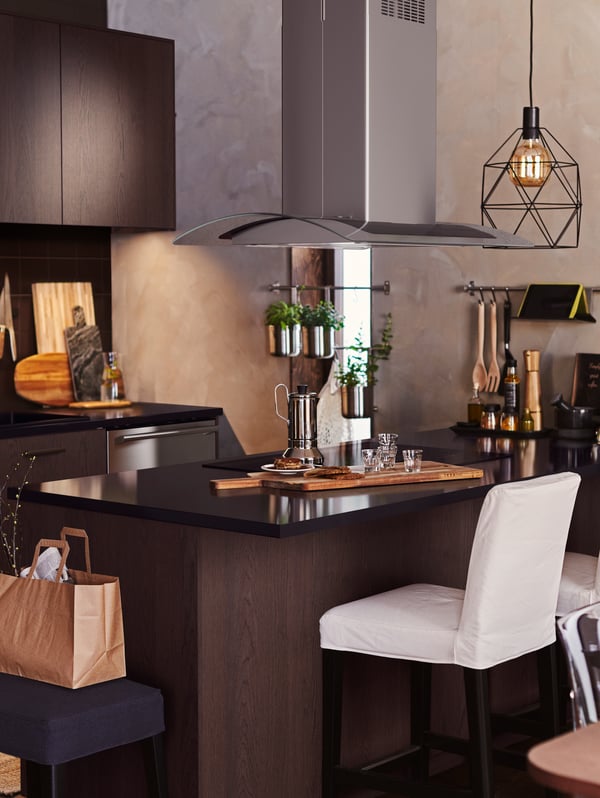 Cocina de madera oscura con una isla que tiene una lámpara de techo con foco BRUNSTA.  En la barra hay una cafetera y vasos.