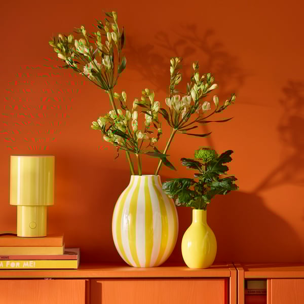 A striped white and yellow BLODBJÖRK vase sits next to a smaller yellow vase on a reddish cabinet with sliding doors.
