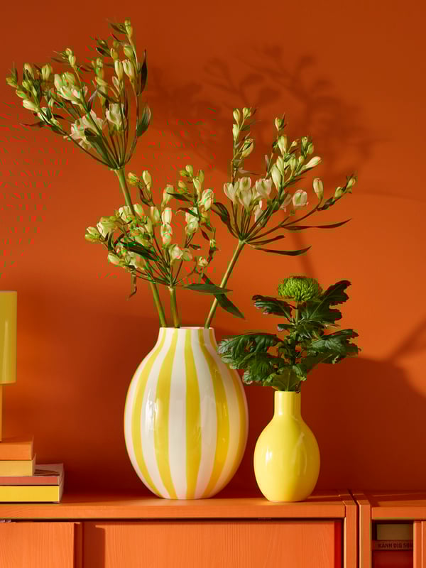 A striped white and yellow BLODBJÖRK vase sits next to a smaller yellow vase on a reddish cabinet with sliding doors.