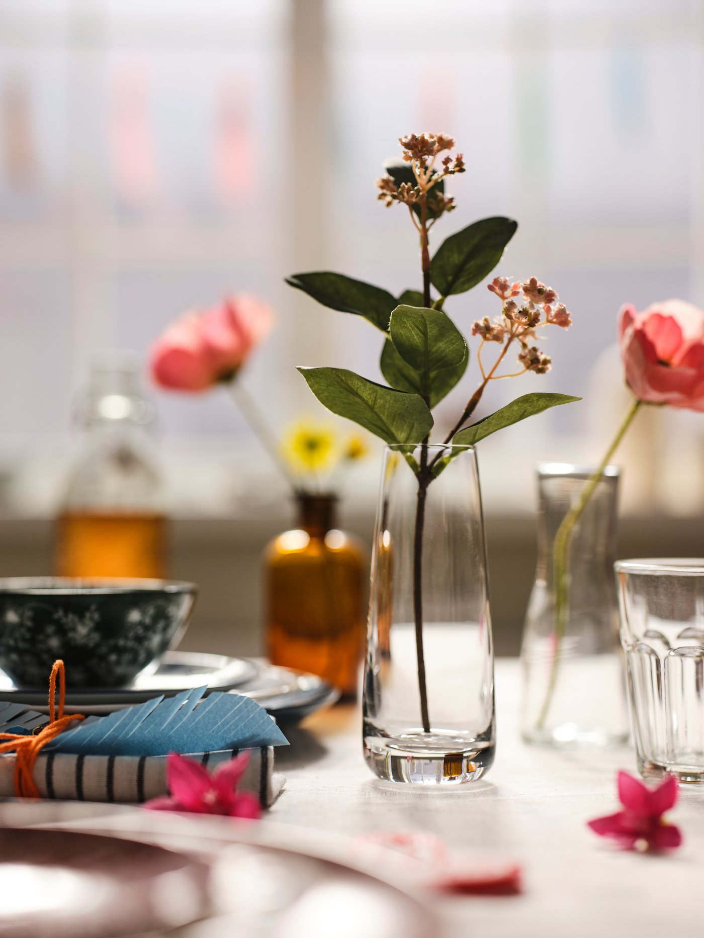 Comedor con varias flores artificiales colocadas en floreros de diferentes formas junto a un vaso y un bowl.