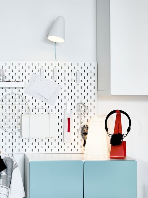 Espace de travail moderne avec panneau perforé blanc, applique à DEL, lampe de table, support pour casque d’écoute, armoire murale, tablette et range-lettres.