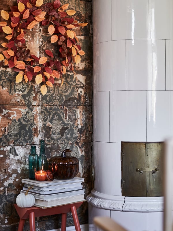 A HÖSTAGILLE artificial wreath in mixed colours adorns a rustic wall, set amidst decorative items, some books and a candle.