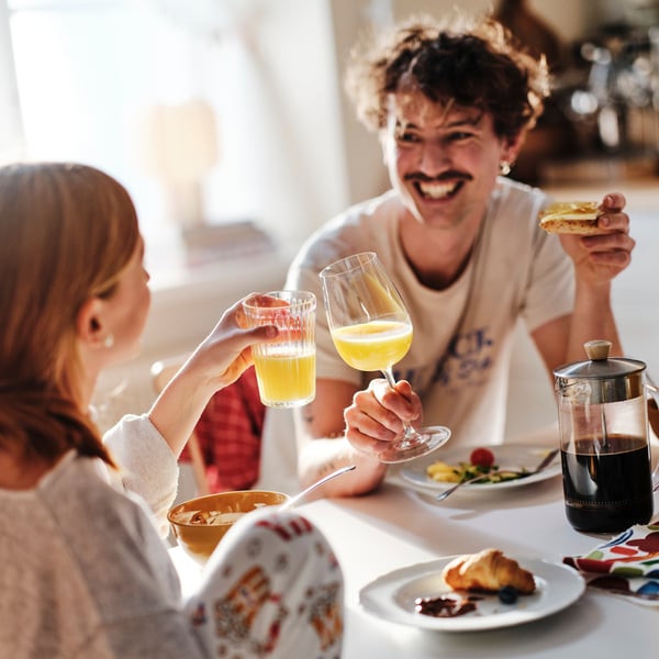 Un père souriant et sa fille adolescente sont assis à une table où ils prennent le déjeuner et trinquent avec leurs verres de jus d’orange.