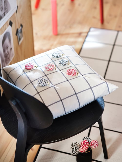 yellow with cushion cover with checkered pattern, on chair, with candy positioned in the squares, and rug on the floor.