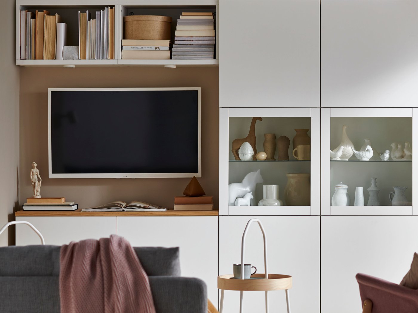 En BESTÅ opbevaringsløsning i hvid med vitrinelåger og et tv.