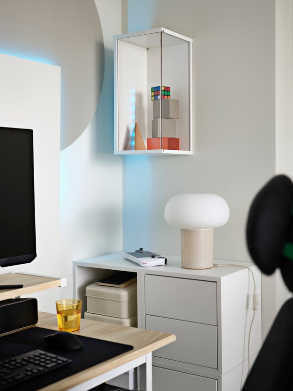 A white BRÄNNBOLL wall-mounted display cabinet with transparent plastic panels is vertical on wall and holds various cubes. 