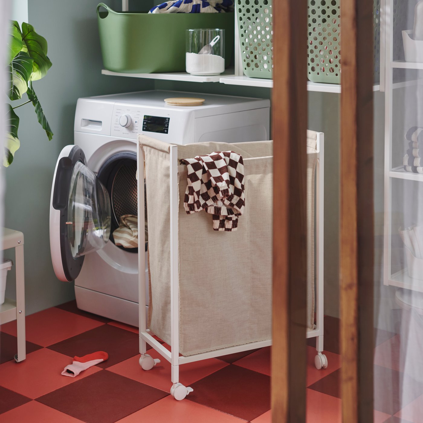 An 80-liter ENHET laundry bag with castors has clothes hanging over the top, by a washing machine in an enclosed balcony.