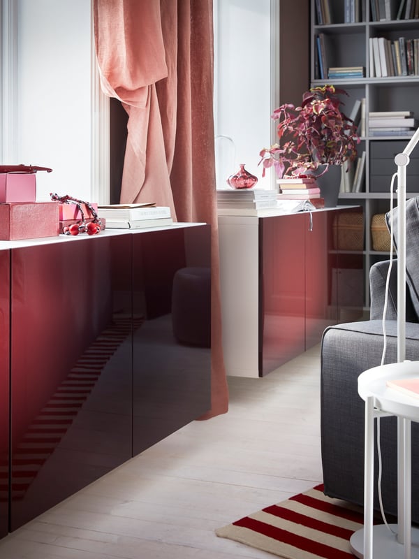 A BESTÅ cabinet combination with high-gloss doors in dark red-brown is wall-mounted under a window.