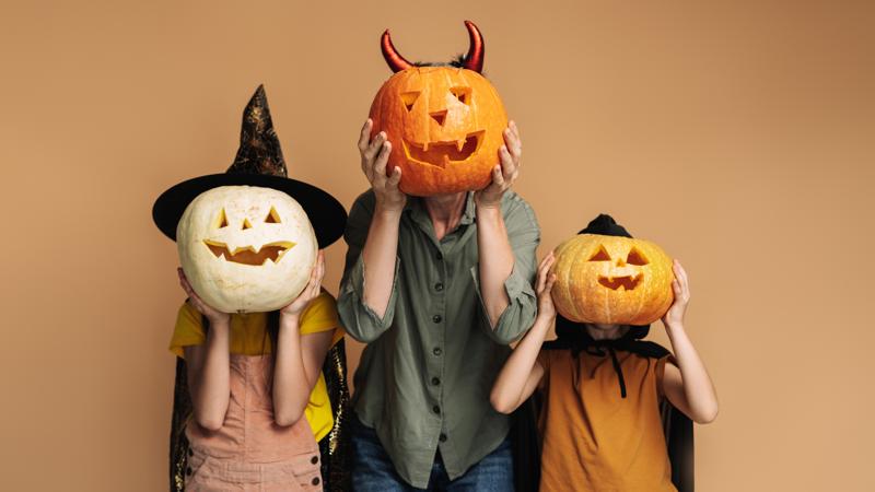 Ein Erwachsener und zwei Kinder, die für Halloween gekleidet sind und einen Kürbis vor ihr Gesicht halten.